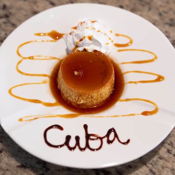 Cuban flan dessert with caramel sauce and whipped cream, with "Cuba" written in chocolate.