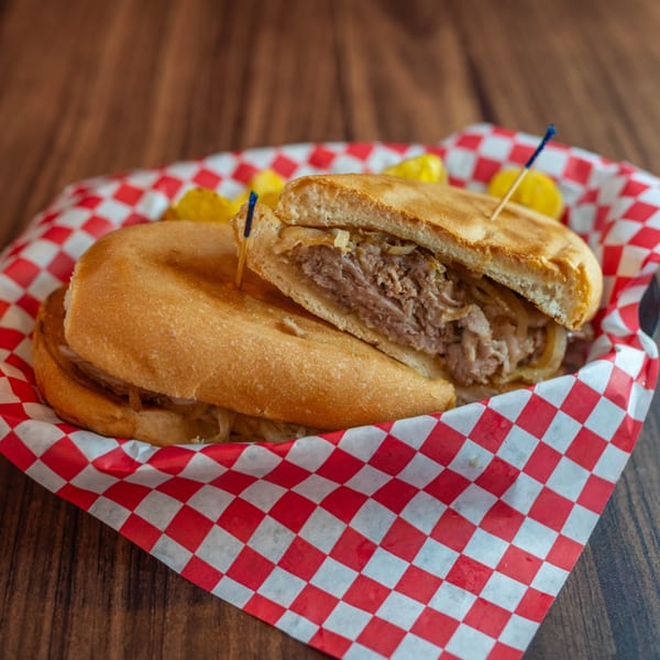 A Cuban sandwich with shredded meat and onions, served in a red and white checkered paper-lined basket.