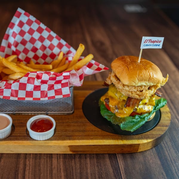 El Tropico Cuban Cuisine burger with fries, ketchup, and sauce on a wooden board.