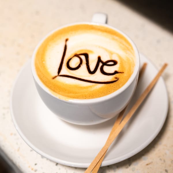 A white cup of Cuban coffee with "love" written in chocolate on the foam, on a white saucer.