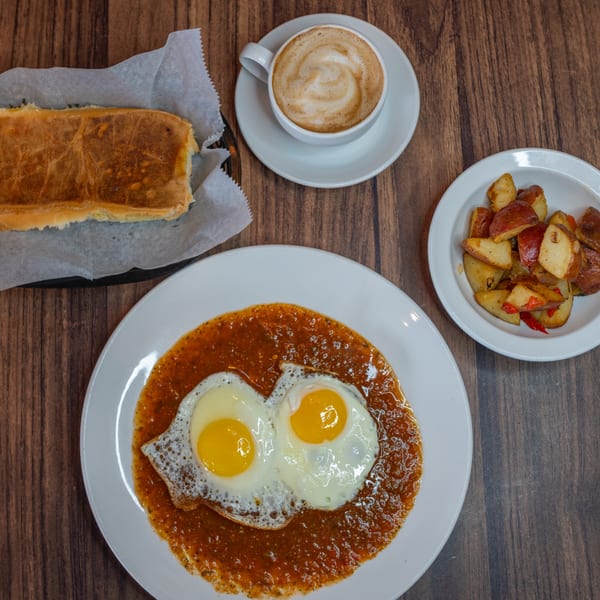 Cuban breakfast with fried eggs in sauce, roasted potatoes, toasted bread, and a latte.